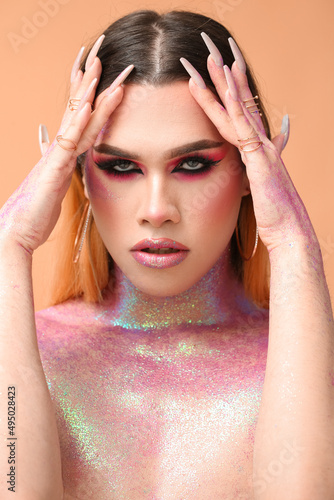 Fashionable young transgender woman with glitters on body against color background