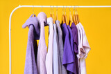 Rack with clothes in purple shades on yellow background, closeup