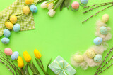 Frame made of painted Easter eggs, tulip flowers, gift box and willow branches on green background