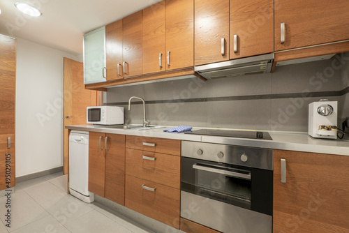 Photo of a kitchen with wooden furniture with stainless steel countertops, matching appliances, ceramic hob, extractor hood and undermount oven