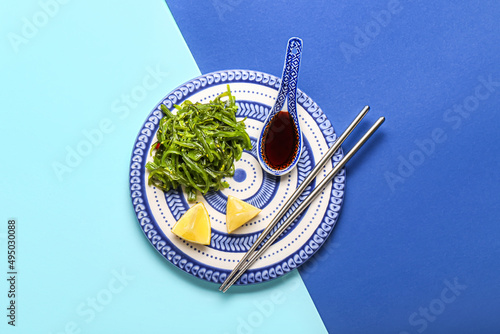 Plate with healthy seaweed salad and sauce on blue background