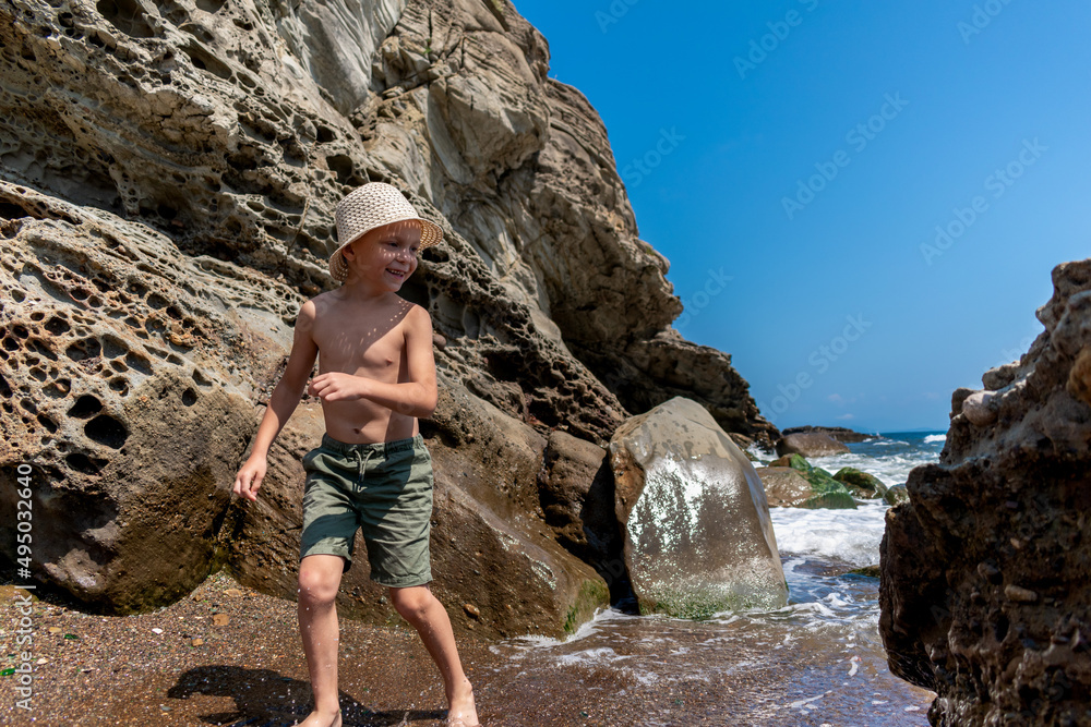 Little boy in a straw hat plays with a sea wave.