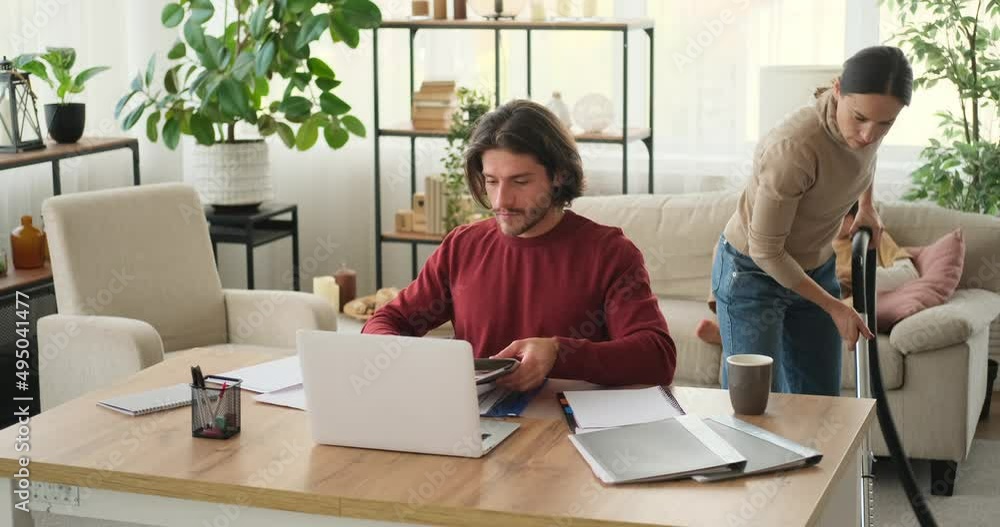 Woman asking working husband to get up while vacuum cleaning at home Woman asking working husband to get up while vacuum cleaning at home