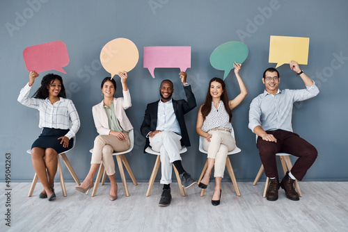 Its a hot topic in the business world right now. Portrait of a group of businesspeople holding speech bubbles while sitting in line against a grey background.