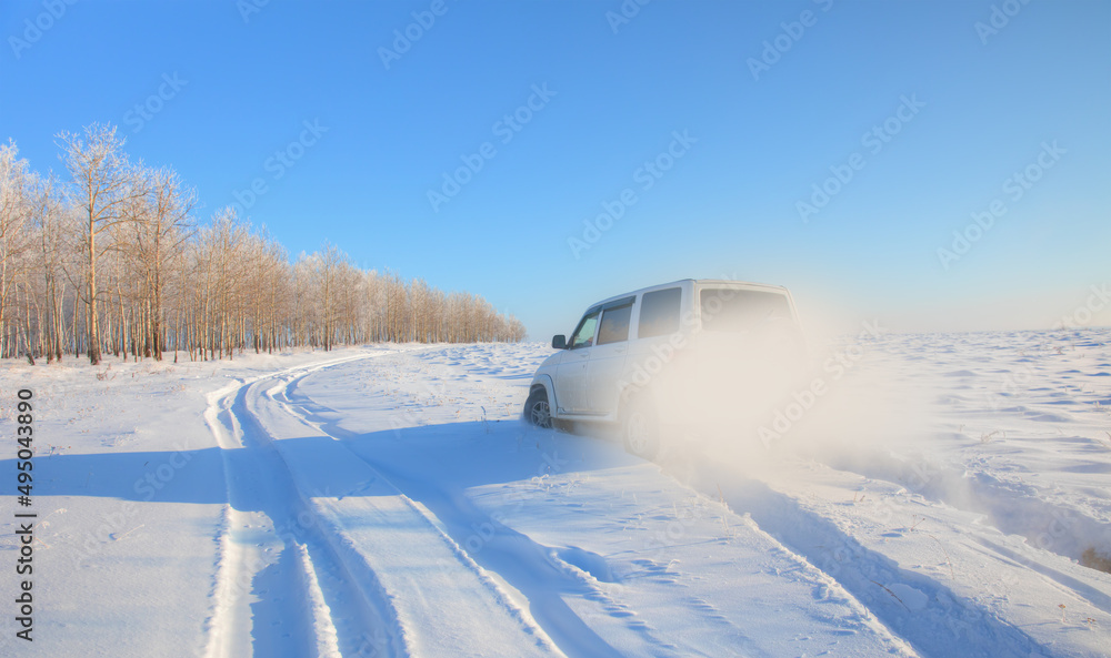An SUV car riding in a field covered with snow off-road snowy trees in the background An SUV car riding in a field covered with snow off-road snowy trees in the background