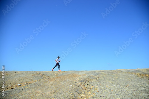 A man in a white shirt is jogging against a beautiful blue belly background.