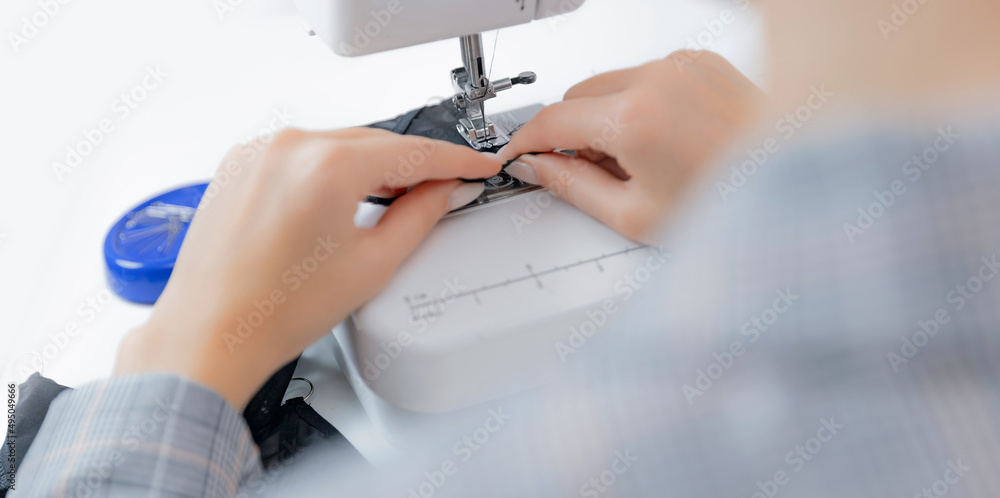 Closeup detail of sewing machine and hand of seamstress tailor woman working, white background banner