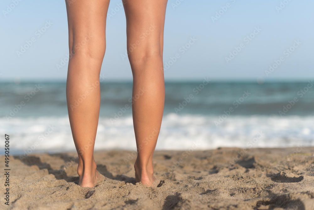 Female barefoot legs on sandy beach near waving sea Female barefoot legs on sandy beach near waving sea