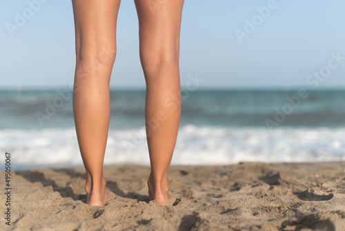 Female barefoot legs on sandy beach near waving sea