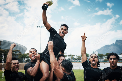 Theyre not just any team theyre rugby cup winners. Cropped shot of a handsome young rugby player holding up a trophy while celebrating with his team on the field.