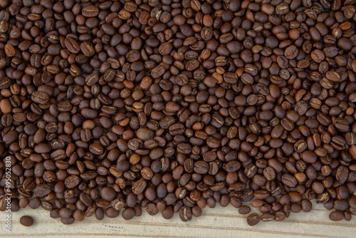 Roasted coffee beans on a light brown wooden floor.
