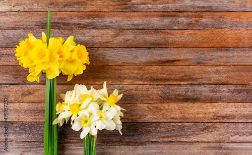 a bouquets of white and yellow narcissus flowers on a brown wooden background with a copy space