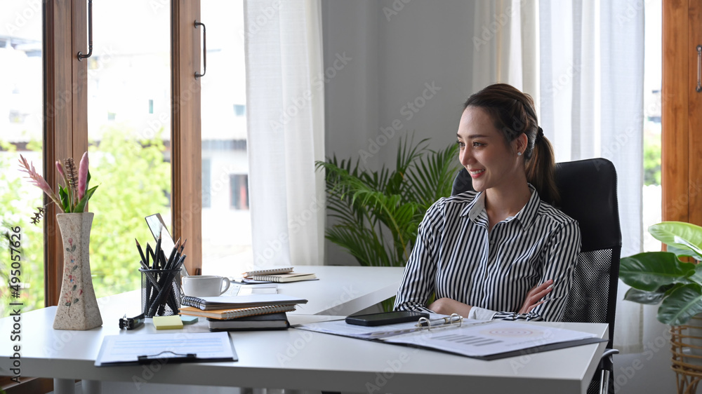 Thoughtful businesswoman team leader sitting at workplace and looking through window.