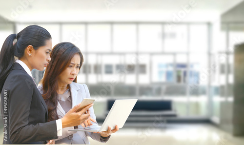 teen age worker holding mobile phone in hand talk to senior worker working with laptop while the woman serious about inter net can not be connected