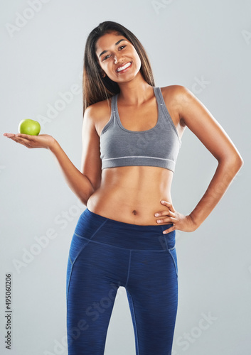 What they say about an apple a day is true. Cropped studio portrait of an attractive young woman holding an apple against a gray background.