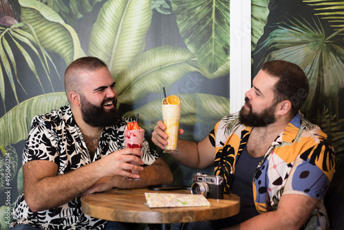 Two gay men enjoying their vacation together. They are happy toasting with a cocktail. Summer and travel as a couple.