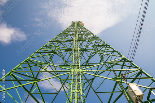 Green high telecommunication telecom tower in sunny day blue sky background. Communication technology, data networking concept.