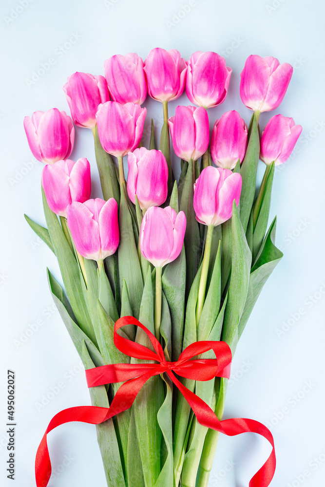 Fototapeta premium Bunch of beautiful pink white tulips tied with red ribbon on blue background, vertical, top view