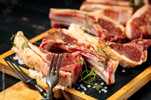 Raw T-bone steak and ribs on a black stone cutting board. Raw meat with spices and herbs. Close-up. Dark wooden background.