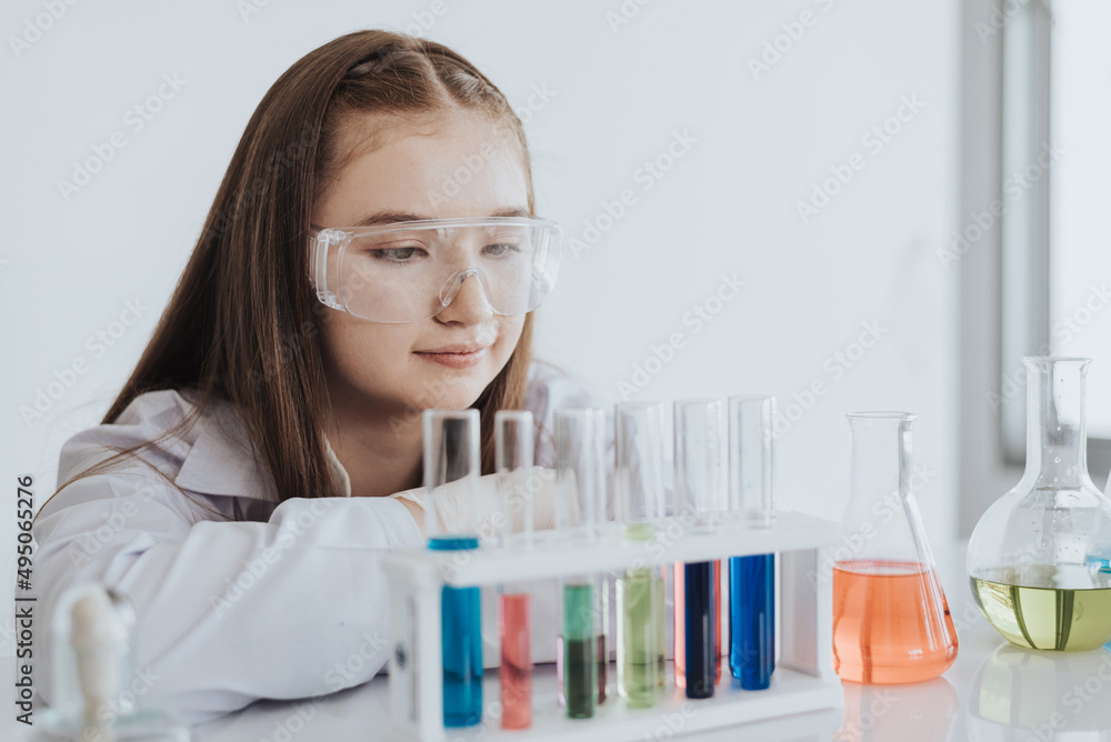 Caucasian girl student learning a chemical experiment in science class. Cute little girl looking test tube while learning chemistry class in white laboratory room. Caucasian girl student learning a chemical experiment in science class. Cute little girl looking test tube while learning chemistry class in white laboratory room.