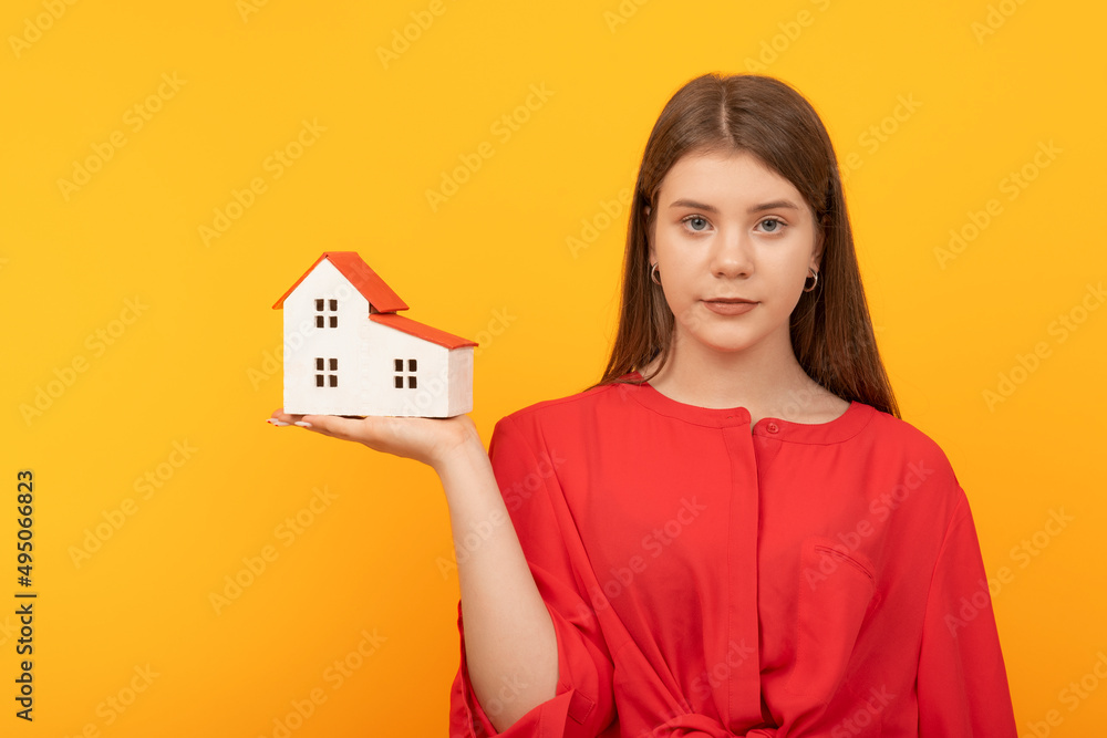 Young pretty woman holds model of house on bright orange background. House insurance concept. Real estate for young families, mortgage Young pretty woman holds model of house on bright orange background. House insurance concept. Real estate for young families, mortgage