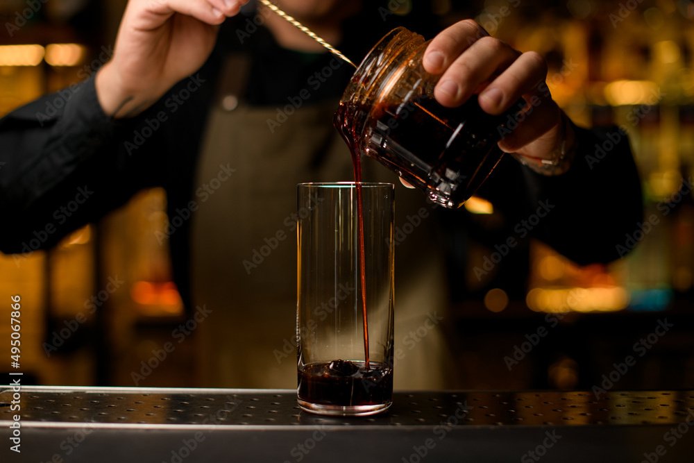 view on transparent cocktail glass into which pouring syrup with spoon from jar