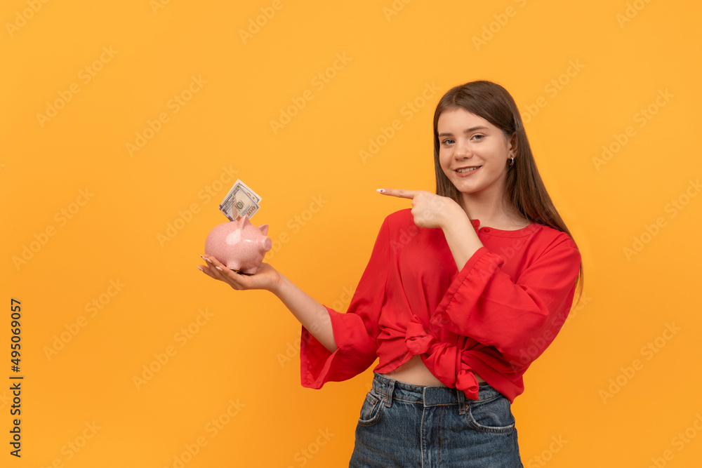 Young woman holds piggy bank and points with finger at it. Concepts of saving money and investments. Young woman holds piggy bank and points with finger at it. Concepts of saving money and investments.