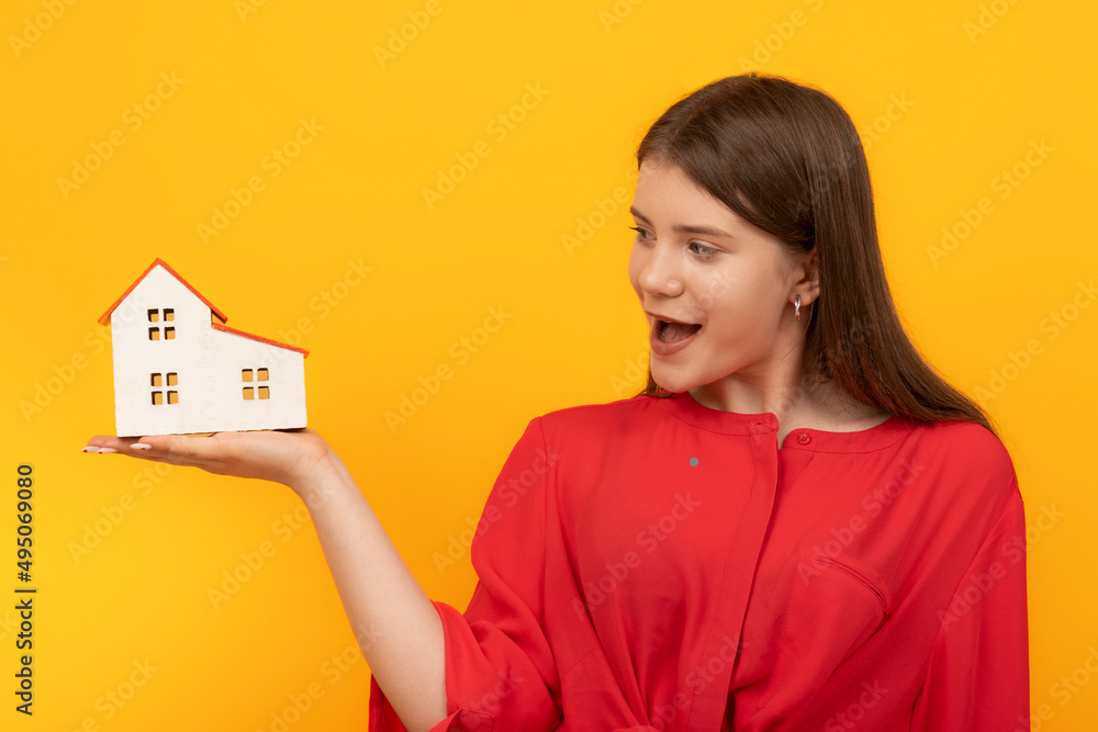 Happy surprised girl holds model of house on palm on bright orange background. Real estate as gift. Winning apartment Happy surprised girl holds model of house on palm on bright orange background. Real estate as gift. Winning apartment