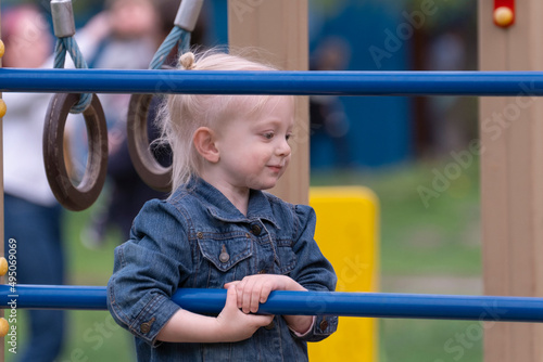 Little blonde girl in denim jacket on sports field. Portrait of child on the childrens playground.