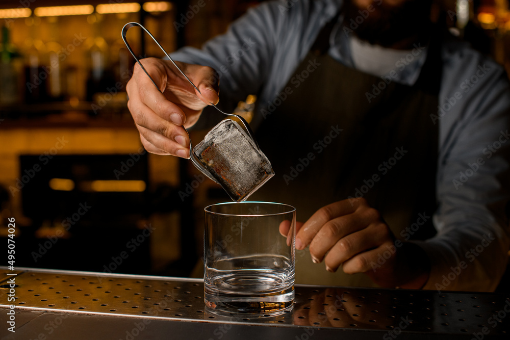 beautiful view on big ice cube held by tongs in male hand over transparent glass
