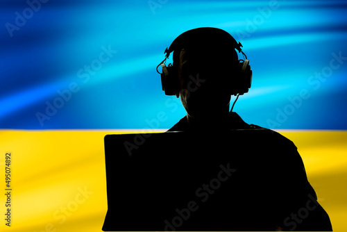 Silhouette of a military man in headphones with a laptop against the background of the flag of Ukraine, selective focus illumination. Concept: security service, eavesdropping secret agent, spy. photo