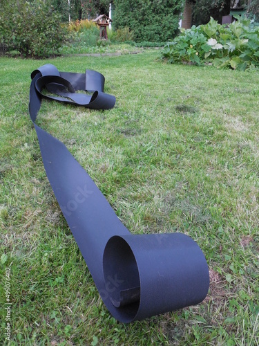 Black flexible border tape to protect the borders of flower beds and flower beds from weeds. The border is unfolded on the grass before you start gardening.