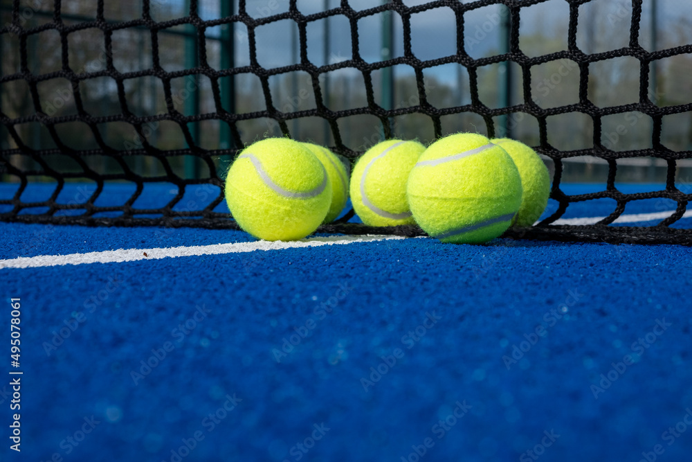 selective focus, five paddle tennis balls near the net of a blue paddle tennis court