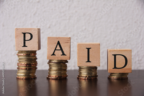 Coins Stack with paid text on wooden blocks - Financial Concept