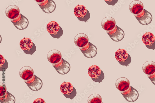Creative pattern made of a half of pomegranate and glass with juice or red wine on pastel beige background. Summer fruit and refreshment  concept. Minimal style. Sunlit flat lay. Top view