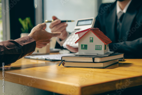 The real estate agent negotiates, discusses the terms of the home purchase contract, and asks the client to sign a contract with the home ode, contract documents, and calculator on the table.