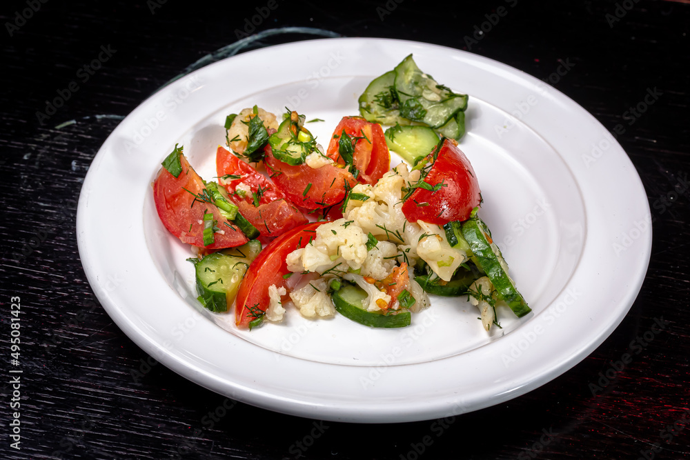 A simple vegetable salad of tomatoes, cucumbers and cauliflower, seasoned with olive oil lies on a white plate A simple vegetable salad of tomatoes, cucumbers and cauliflower, seasoned with olive oil lies on a white plate