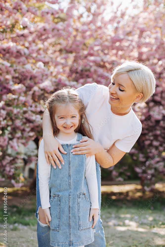 Family (mother and children) in spring city street with pink japanese cherry trees blossom (Uzhhorod City, Ukraine). Sakura blossomed. Young mother with her child have fun in the park near the sakura. Family (mother and children) in spring city street with pink japanese cherry trees blossom (Uzhhorod City, Ukraine). Sakura blossomed. Young mother with her child have fun in the park near the sakura.