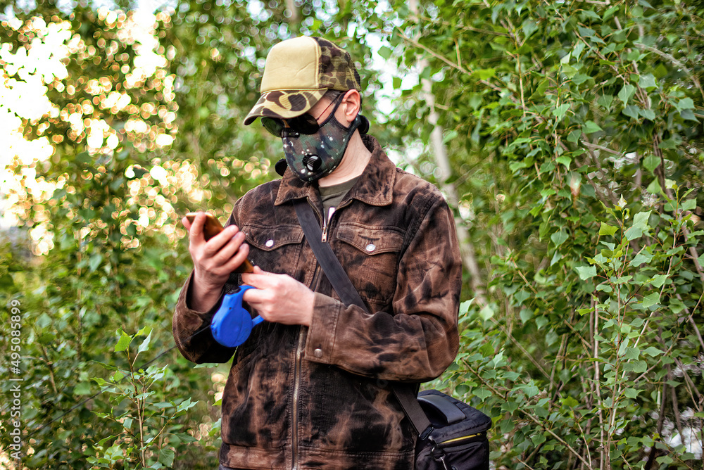 A man wearing respirator mask and dialing a smartphone walking in the forest at COVID-19 period.