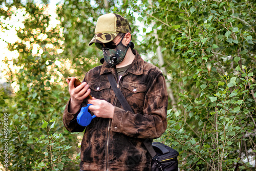 A man wearing respirator mask and dialing a smartphone walking in the forest at COVID-19 period.