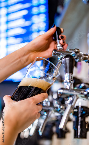 woman bartender hand at beer tap pouring a dark beer in glass serving in a restaurant or pub