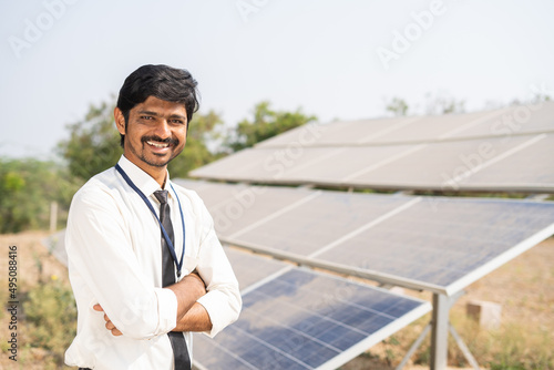Smiling bank officer standing with crossed arms by looking at camera in front of solar panels - concept of successful, renewable energy and investment support for solar installation. © WESTOCK
