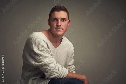 Obraz He can looked right through you. Studio portrait of a confident young man seated against a grey background while looking at the camer.