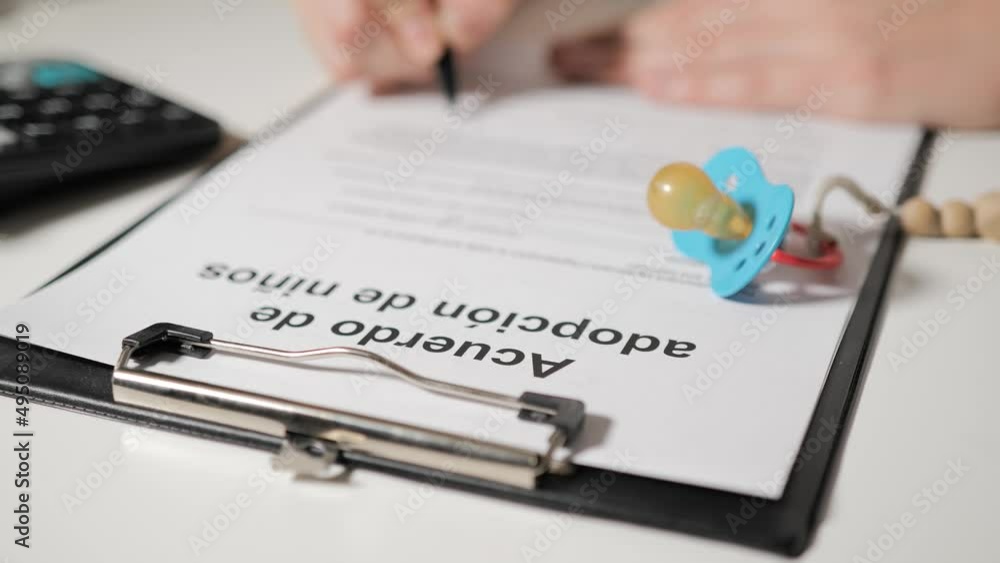 Agreement on the adoption of child in Spanish-speaking languages. Female or male hands sign documents. In the foreground lies baby pacifier. Agreement on the adoption of child in Spanish-speaking languages. Female or male hands sign documents. In the foreground lies baby pacifier.
