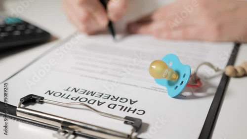 Agreement for the adoption of child. Female or male hands sign documents. In the foreground lies a baby pacifier. photo