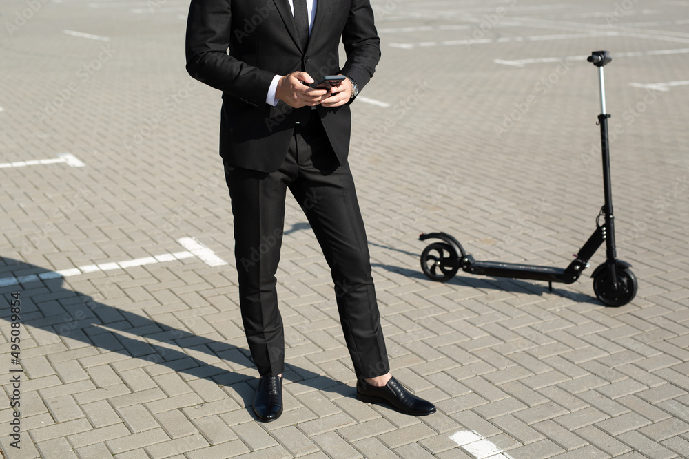 Young handsome businessman in a suit rides an electric scooter and looks at the phone Young handsome businessman in a suit rides an electric scooter and looks at the phone