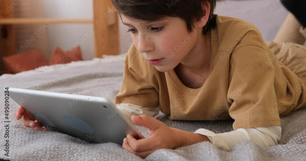 Boy using digital tablet lying on bed at home Boy using digital tablet lying on bed at home