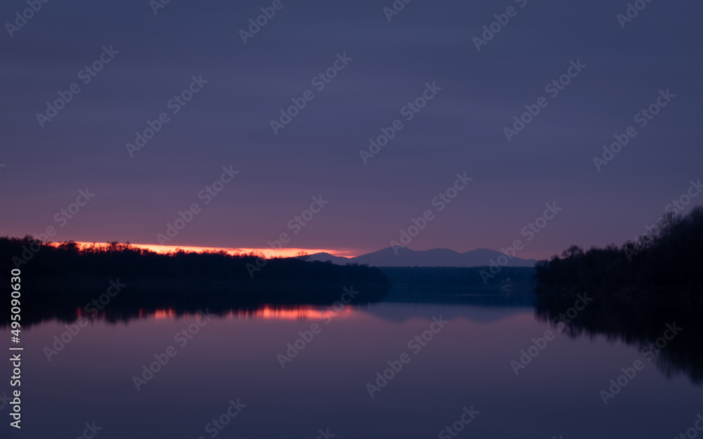 Calm nightfall over Sava river with fading light under clouds and mountain silhouette - natural landscape