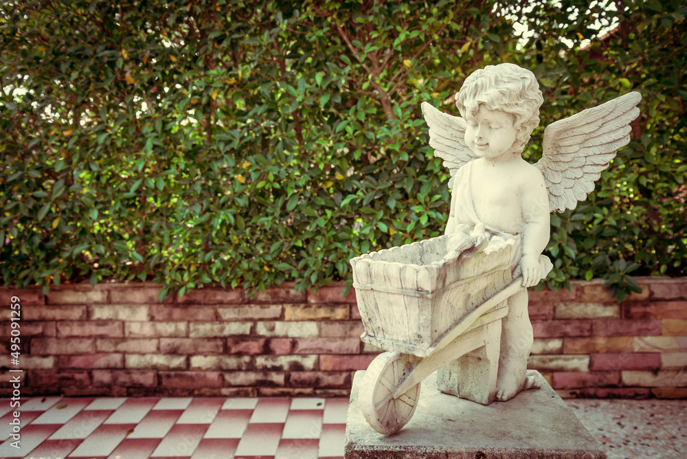 White cute cupid statue in garden with green tree background. Love valentine day concept. White cute cupid statue in garden with green tree background. Love valentine day concept.