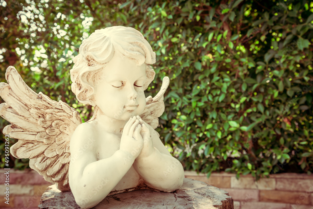White cute cupid statue in garden with green tree background. Love valentine day concept. White cute cupid statue in garden with green tree background. Love valentine day concept.